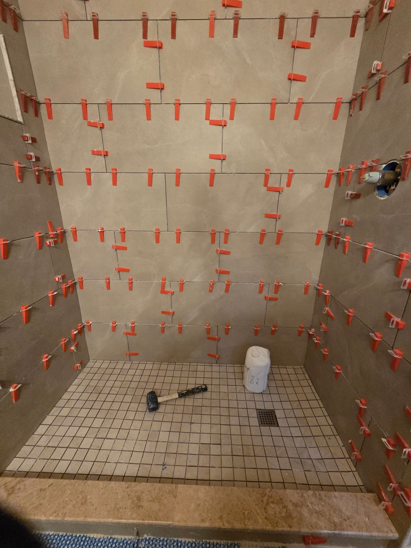 Large-format shower tile being set with leveling clips